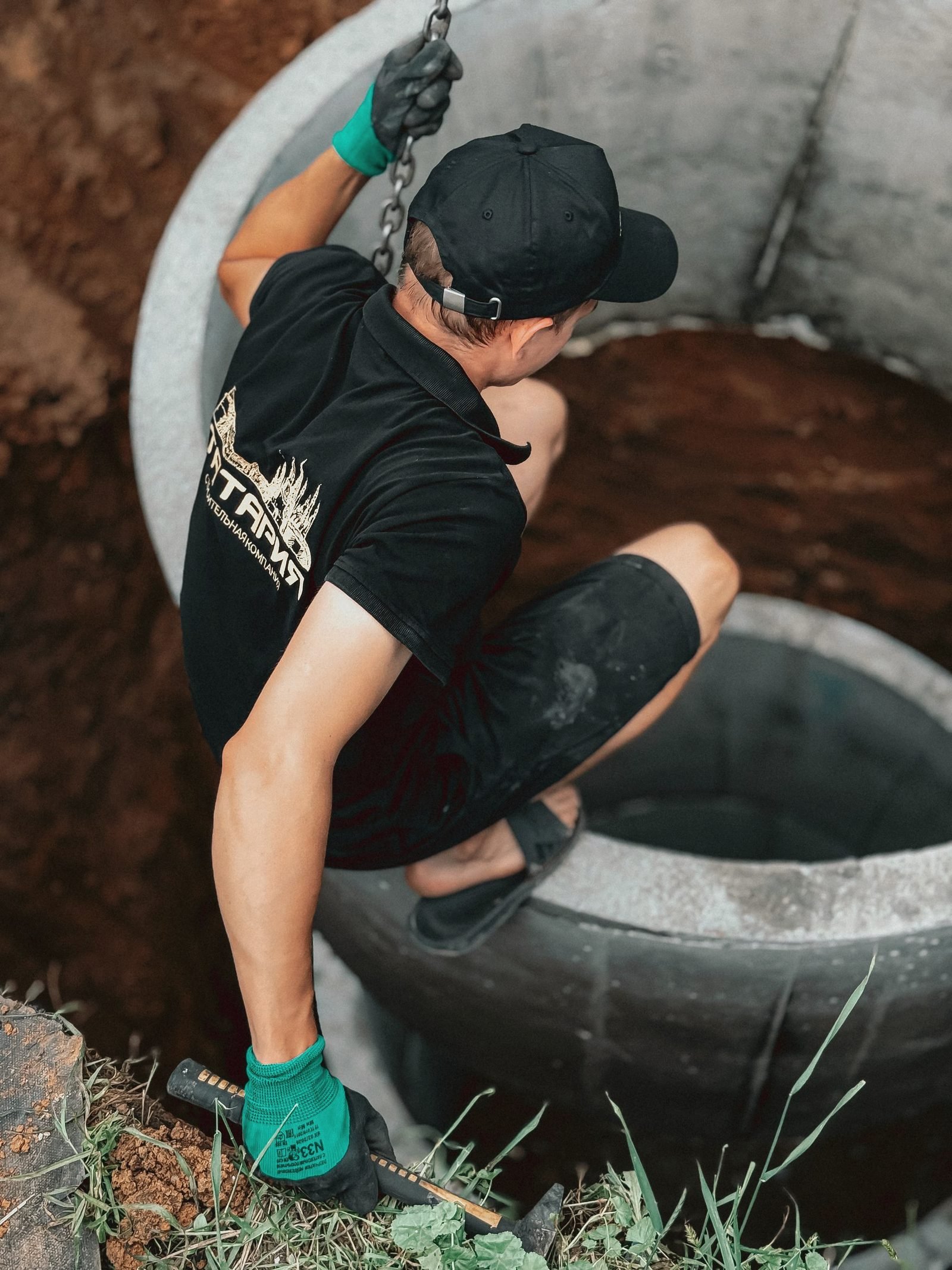A worker kneeling inside a concrete ring set into the ground