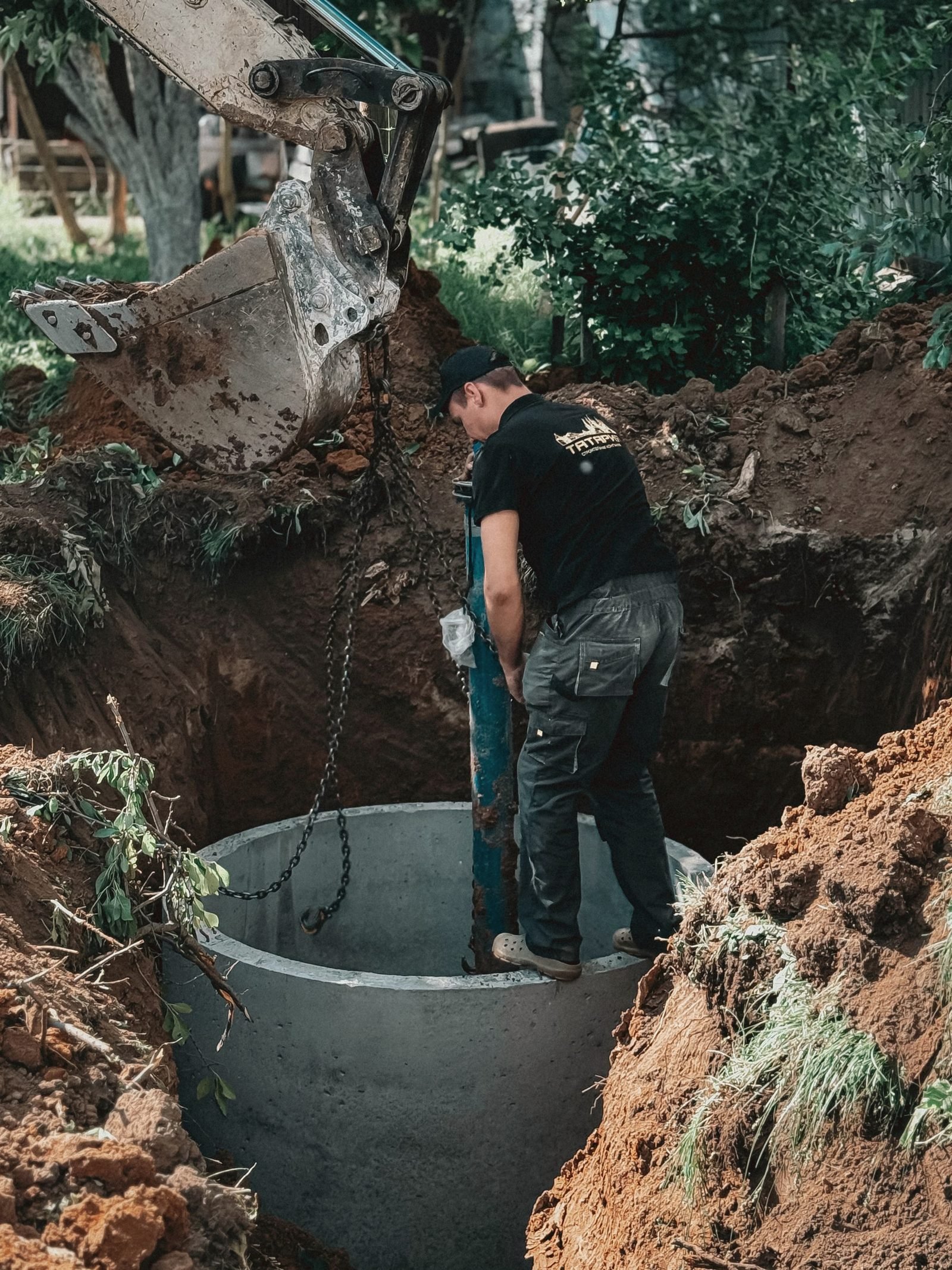 A worker standing in an excavated hole beside a round concrete chamber