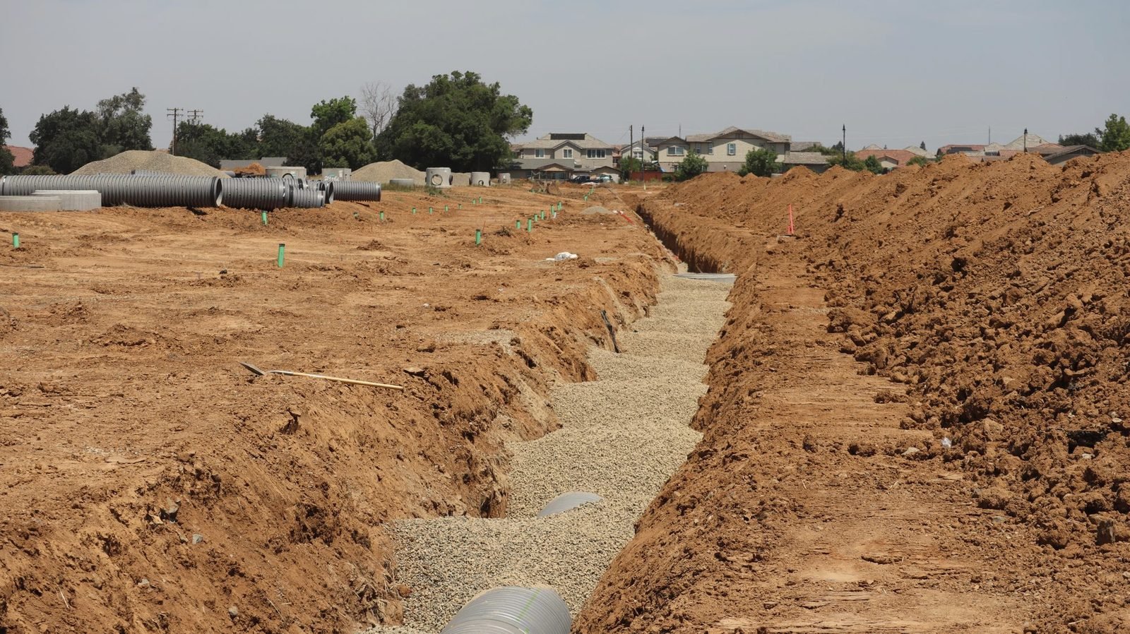 Two long parallel trenches dug in tan soil with gravel along the bottom