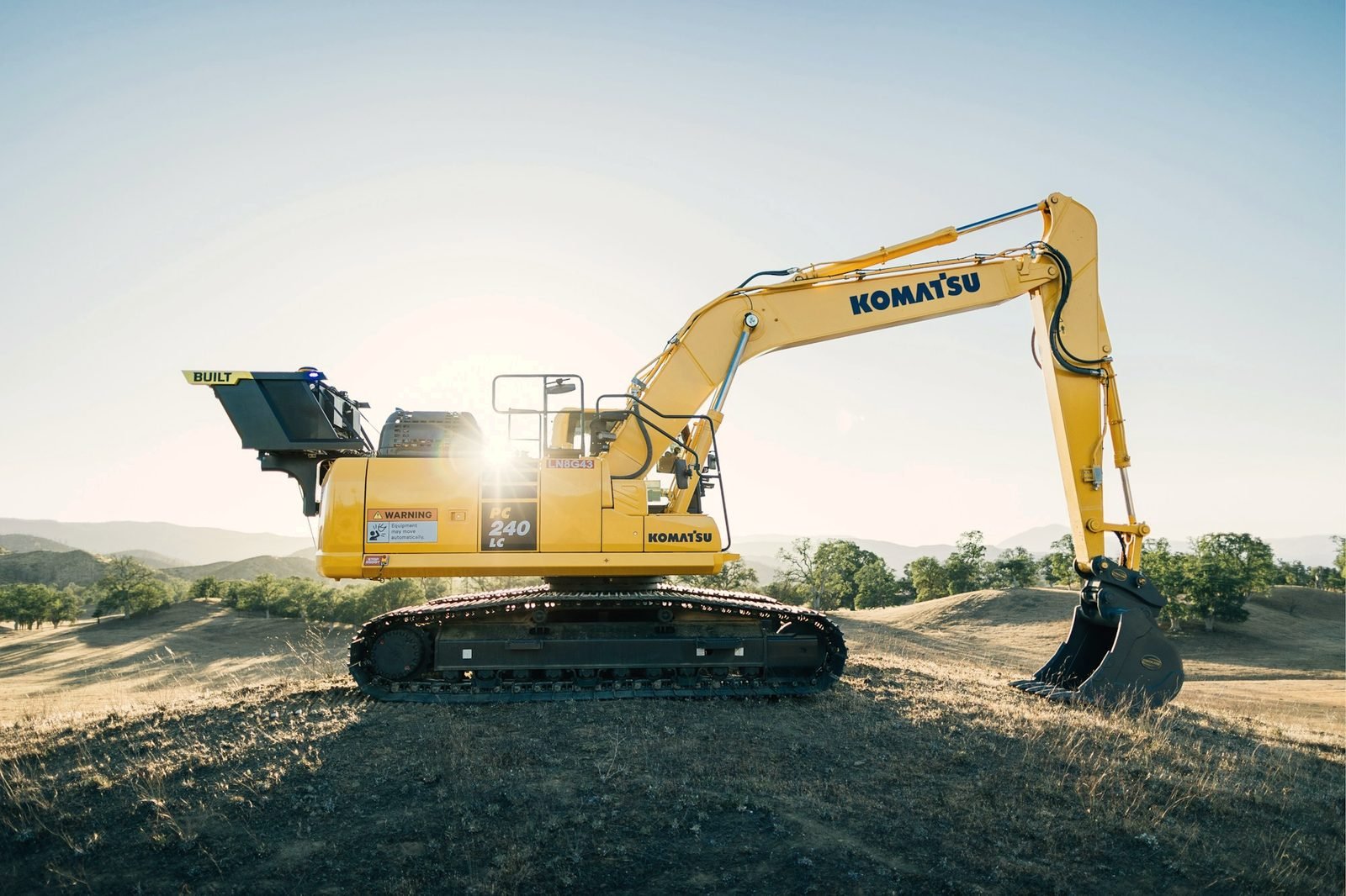 A yellow excavator on a sandy rise at sunrise