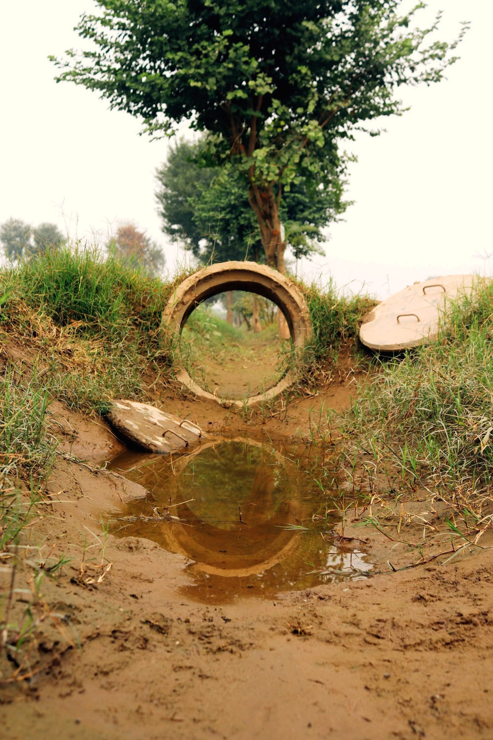 A pipe end sitting in a muddy, water-filled cut in the ground